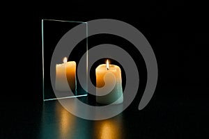 Burning candle and mirror on a black background.