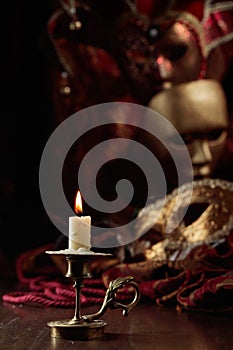 Burning candle in an old brass candlestick and carnival masks