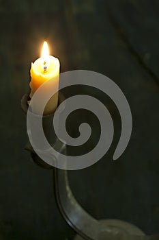 A burning candle in an old pewter metal candle holder