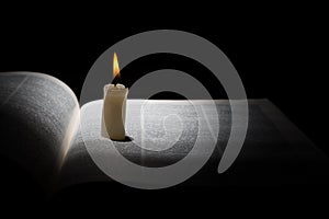 Burning candle on opened book on black background