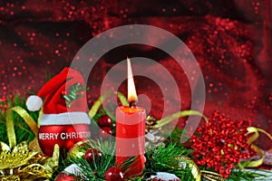 Burning candle with red bauble with Santa hat and Christmas decorations