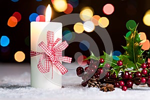 Burning candle with red bow, in snow, with defocussed fairy lights, bokeh