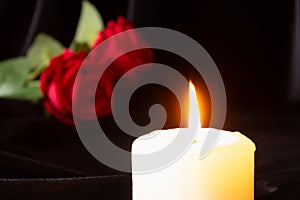 A burning candle and a red rose on a black background. The concept of condolences, mourning, and funerals