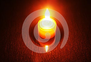 Burning candle on a reflective table. Visible candle and its ref