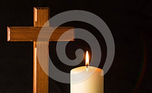 Burning candle under wooden cross in a cemetery against black background.