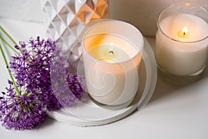 Burning candle and violet allium flowers on white tray