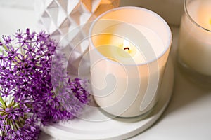 Burning candle and violet allium flowers on white tray