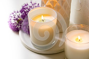 Burning candle and violet allium flowers on white tray