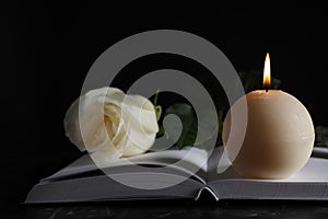 Burning candle, white  and book on table in darkness, closeup. Funeral symbol
