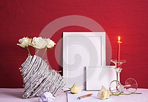 Burning candle, writing materials, roses in a vase, white photo frames, wooden heart on a red background