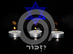 Burning candles with background blurred Jewish star Magen David and blurred Hebrew text translation - I will remember