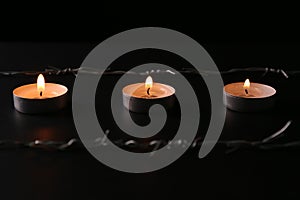 Burning candles and barbed wire on black background. Holocaust memory day