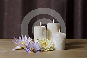 Burning candles and beautiful waterlily on a wooden floor