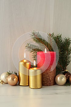 Burning candles with Christmas baubles and fir tree branch on table against wooden background