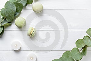 Burning candles with eucalyptus branches and macaroons on white wooden background