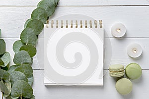 Burning candles with eucalyptus branches, notebook and macaroons on white wooden background