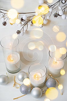 Burning candles with festive bokeh and silver balls on a light background.