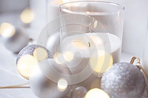 Burning candles with festive bokeh and silver balls on a light background.