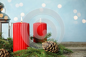 Burning candles and fir branches on wooden table against light blue background, bokeh effect. Space for text