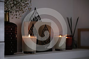 Burning candles. flowers and decor on white shelf