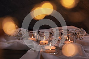 Burning candles and flowers on table against blurred festive lights