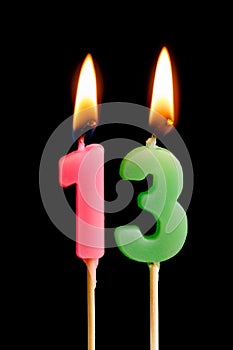Burning candles in the form of 13 thirteen figures numbers, dates for cake isolated on black background. The concept of celebrat
