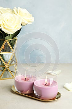 Burning candles in glass holders and roses on light table