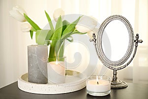 Burning candles, mirror and flowers on black table indoors