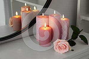 Burning candles and rose on white console table near mirror