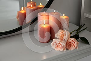 Burning candles and roses on white console table near mirror, space for text