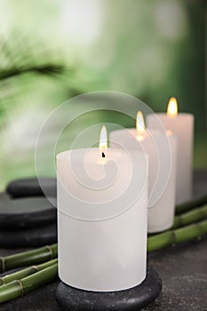 Burning candles, spa stones and bamboo sprouts on grey table against green background
