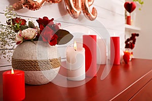 Burning candles and vase with flowers on red table indoors. Valentine`s Day celebration