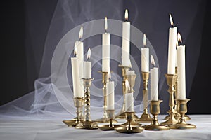 Burning candles in vintage metal candlesticks on white table against abstract white tulle material  background.