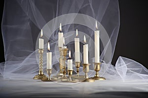 Burning candles in vintage metal candlesticks on white table against abstract white tulle material  background.