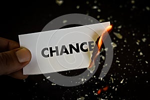 Burning chance, human hand holding the word chance written on a paper burning with flame and ashes on a black background