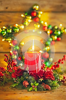 Burning Christmas red candle and  festive Christmas arrangement on a wooden table