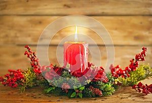 Burning Christmas red candle and  festive Christmas arrangement on a wooden table