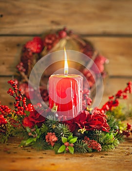 Burning Christmas red candle and  festive Christmas arrangement on a wooden table