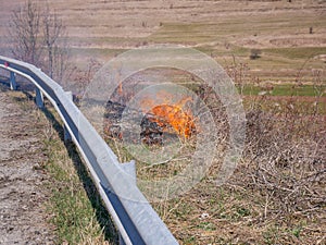 Burning dried vegetation near roadside, negligent people setting up the fire photo