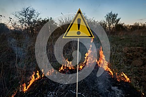 Burning dry grass in field and warning sign