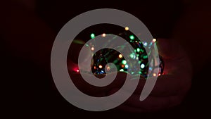 Burning festive christmas garland with lights in male hands on a dark background.Selective focus, blur, retro-toning