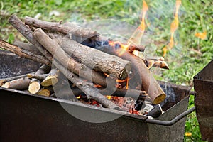 Burning firewood in barbecue grill on green grass. Rest, weekend