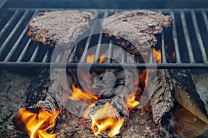 Burning firewood with flame through bbq grill grates and steaks on it