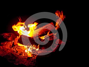 Burning firewood at night. Bonfire in a camping camp in nature in the mountains. Flames and fiery sparks on a dark