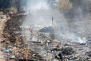 Burning garbage at illegal waste dumo near forest. Black earth and heavy junk smoke. Environmental pollution aftermath concept