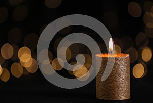 Burning gold candle against blurred lights in darkness
