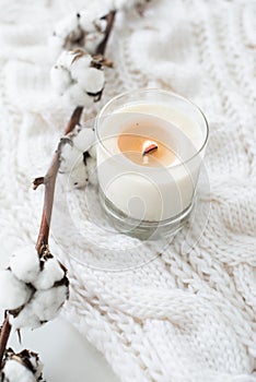Burning hand-made candle with cotton branch on white cozy winter