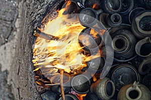 Burning handmade pottery pieces in earthen firing chamber of ancient pit fire kiln replica