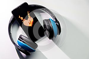 Burning heart symbol with burning flames on a black smartphone screen and blue over ear headphones and copy space
