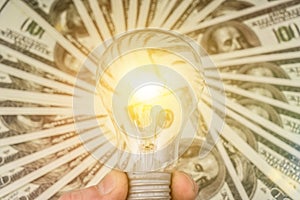 Burning idea lamp in businessman hand on a background of dollars money.